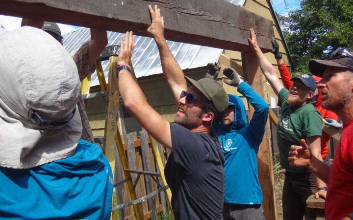 a group of people lift a piece of wood up high while working on a service project